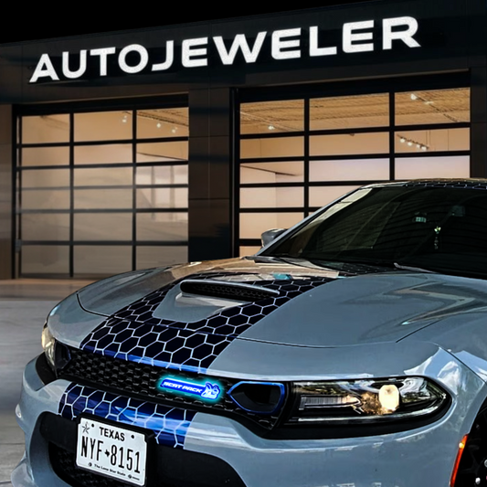 Gray sports car with blue accents in front of a building with 'AUTOJEWELER' sign.