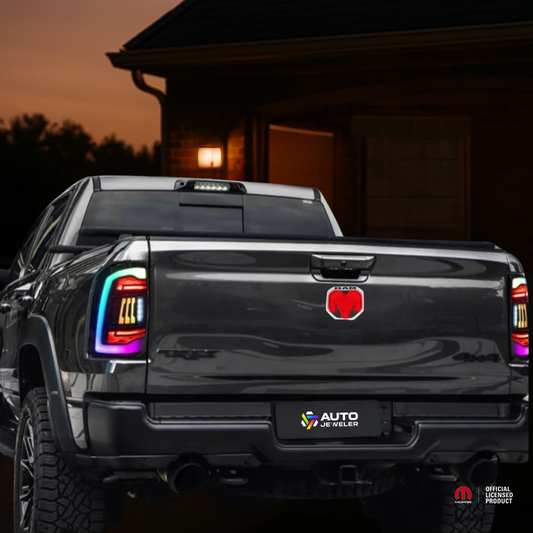 Nighttime rear shot of a RAM truck with the red LED tailgate emblem illuminated and AutoJeweler license plate branding.