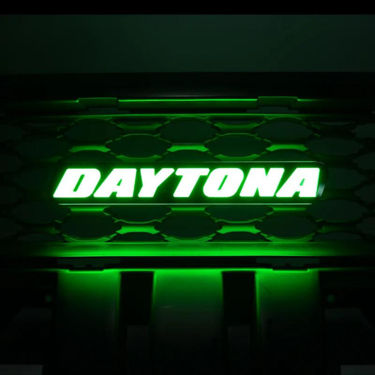 Daytona LED grille emblem illuminated in vivid green lighting mode mounted on black grille background