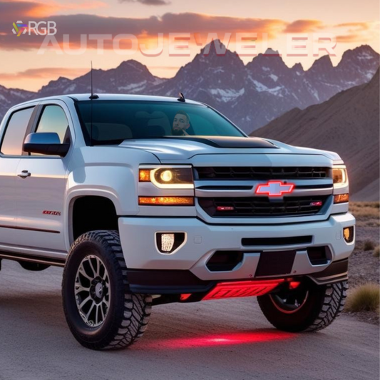 White Chevy Silverado with AutoJeweler RGB LED Bowtie Grille Emblem illuminated in red, parked outdoors at sunset with mountain background.
