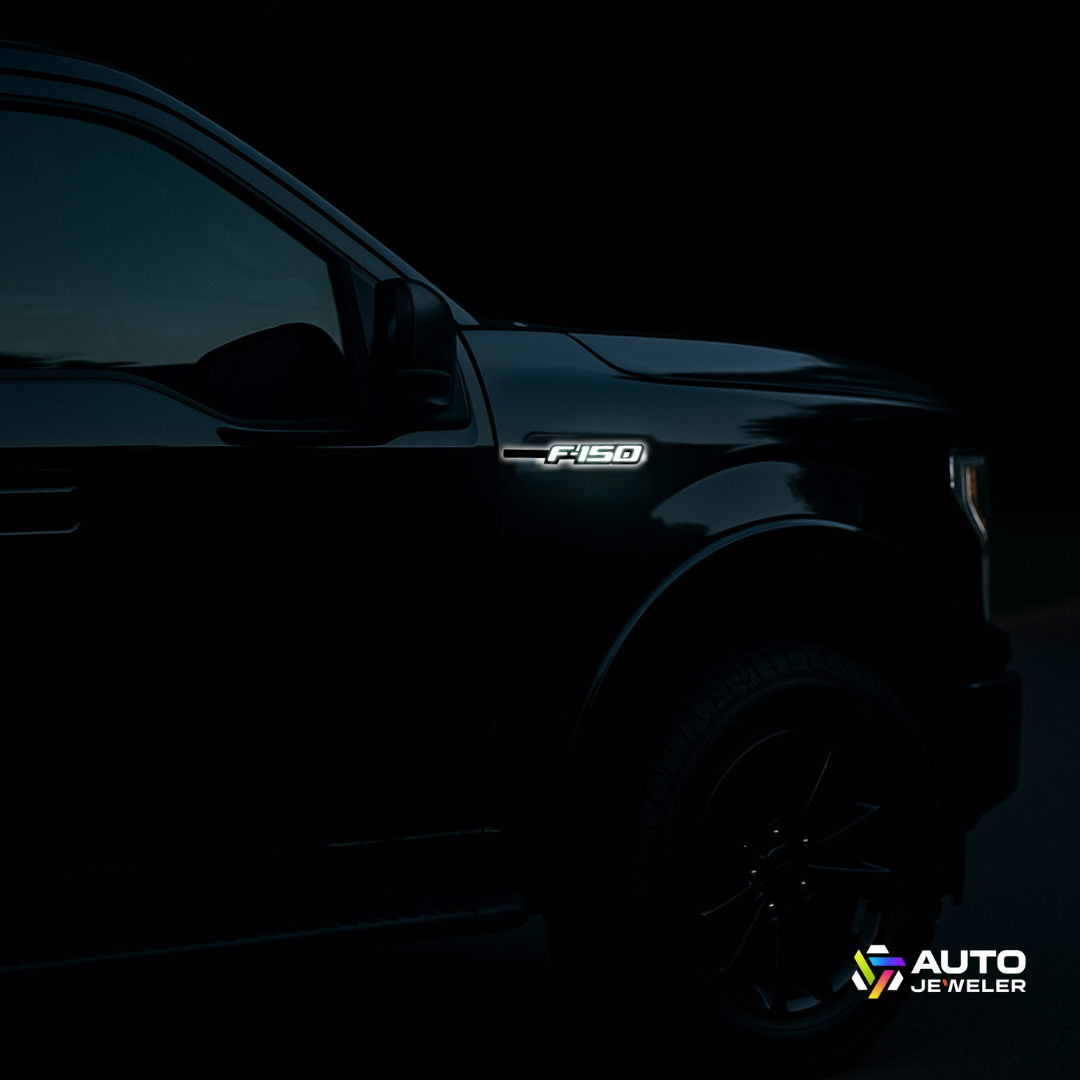 Gloss black LED F-150 fender emblem illuminated at night on a black Ford F-150 truck, side view, with AUTO JEWELER logo.