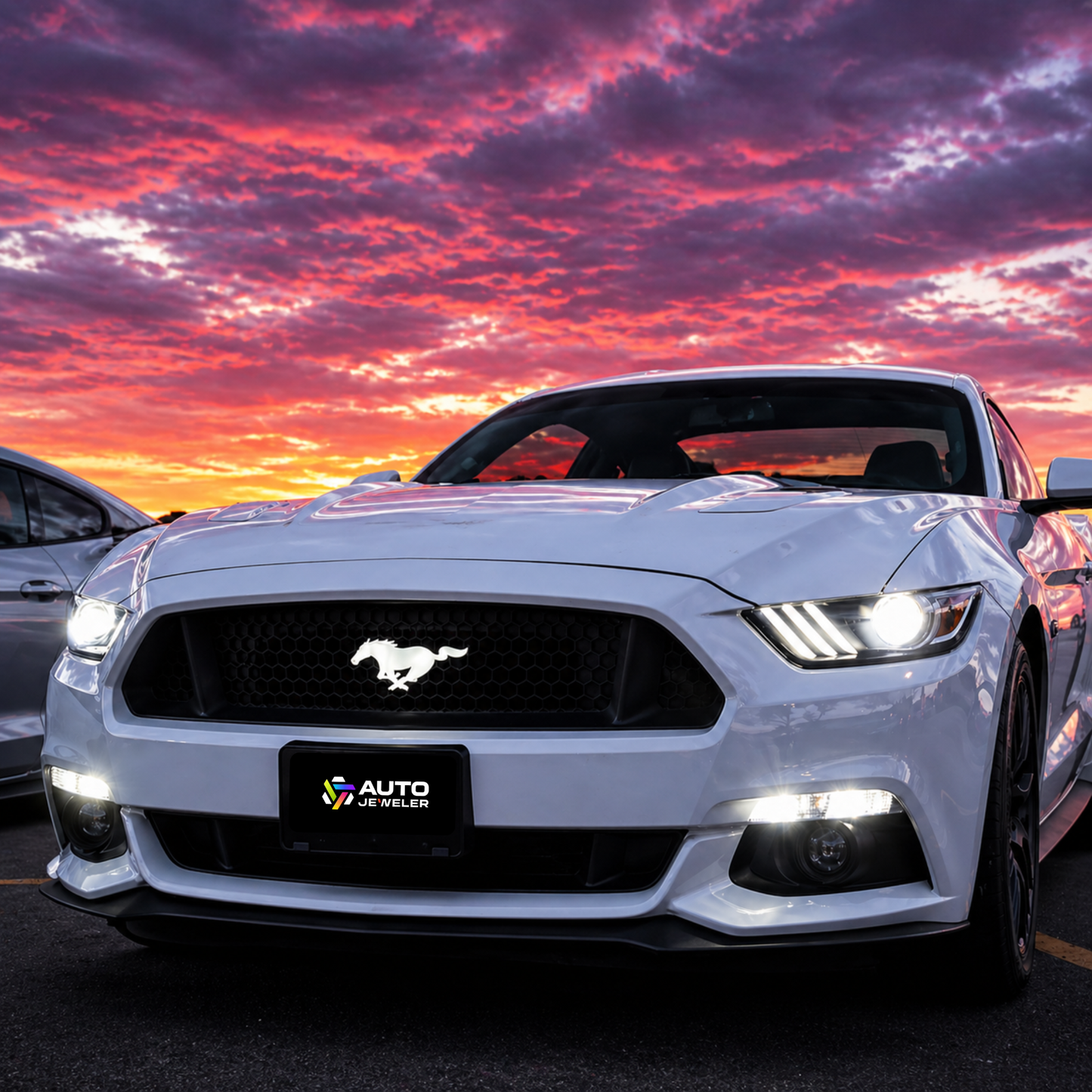 White 2015–2024 Ford Mustang front view at sunset with illuminated pony grille emblem and AutoJeweler branded plate.