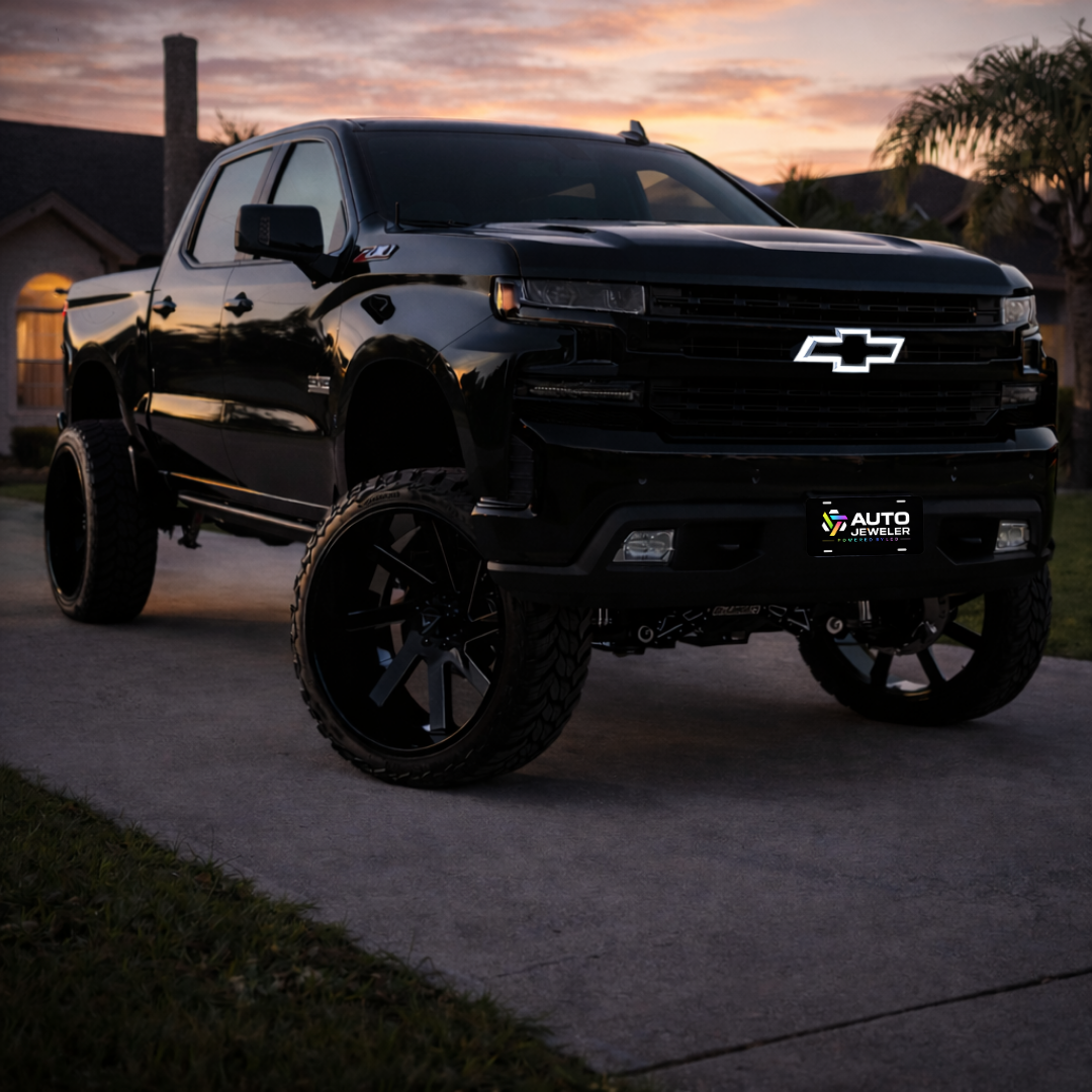 Lifted black 2016–2018 Chevy Silverado 1500 at sunrise with all-black LED bowtie grille emblem installed and illuminated white, front three-quarter lifestyle view