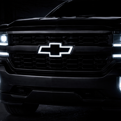 All black LED Chevy bowtie grille emblem with white illumination installed on a 2016–2018 Chevrolet Silverado 1500 with headlights on at night
