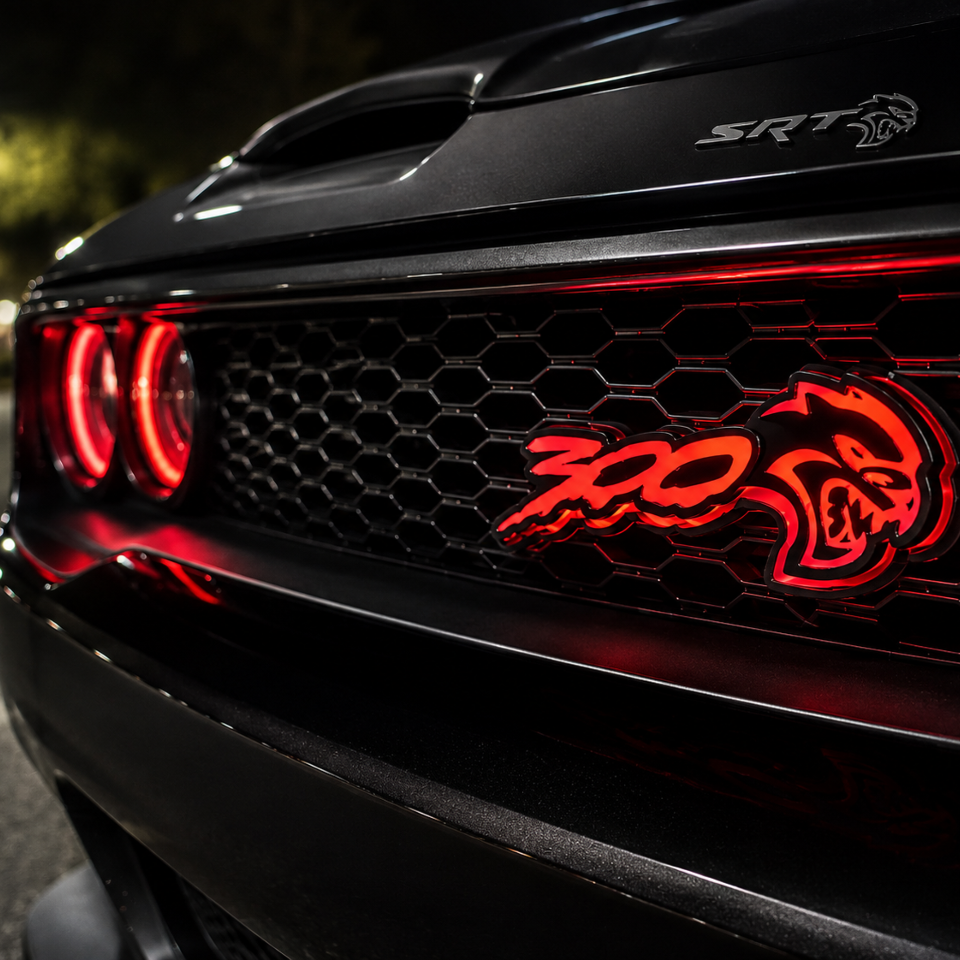300 Hellcat V2 Style Flow Series LED emblem glowing red on a black mesh grille in a nighttime automotive lifestyle photo.
