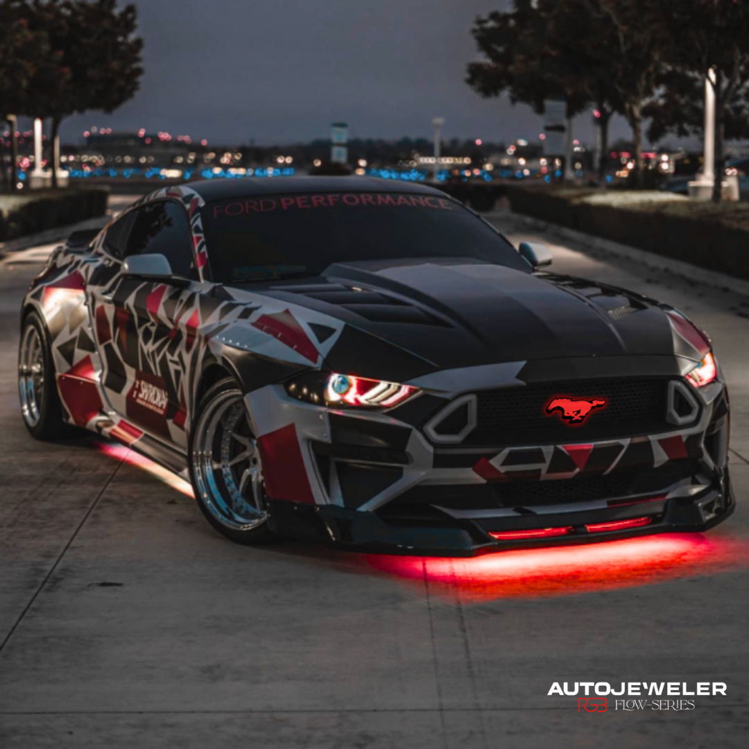 Customized Ford Mustang with LED Pony grille logo illuminated red on a street at night, featuring the AutoJeweler logo.