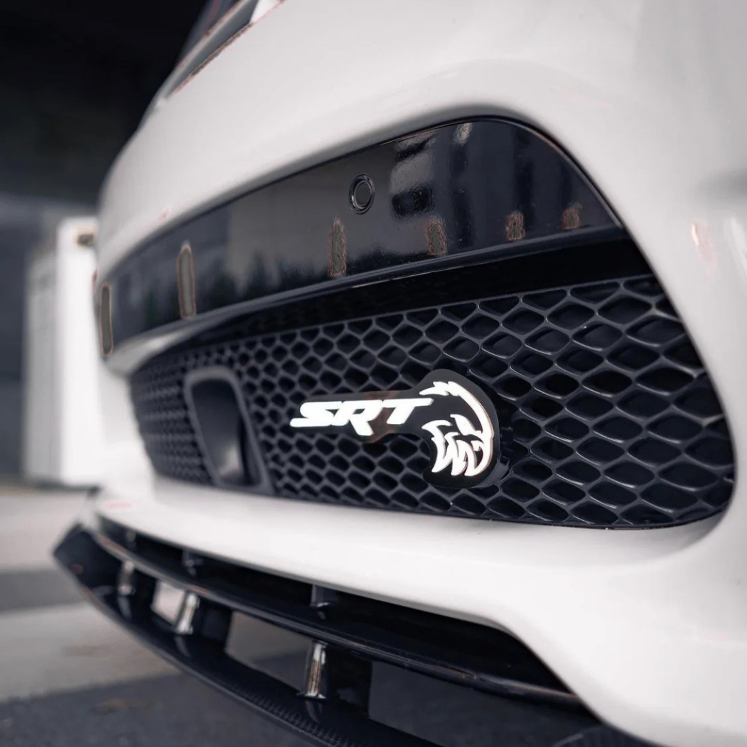 Close-up of AutoJeweler SRT Trackhawk Hellhawk LED grille emblem installed on white Jeep front bumper mesh grille