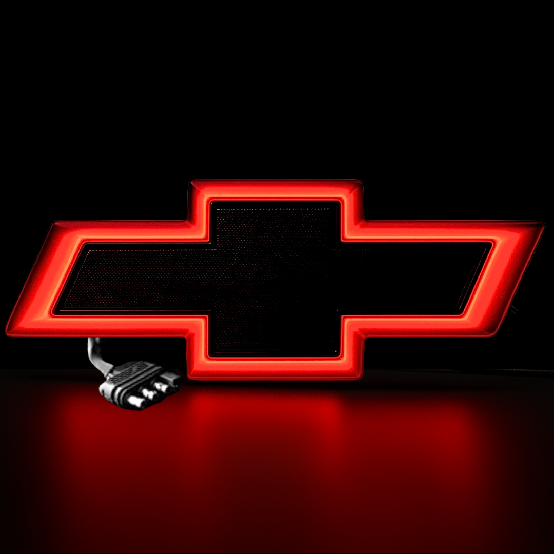 Close-up of red-lit tailgate bowtie emblem on textured surface with 4-pin wiring connector.