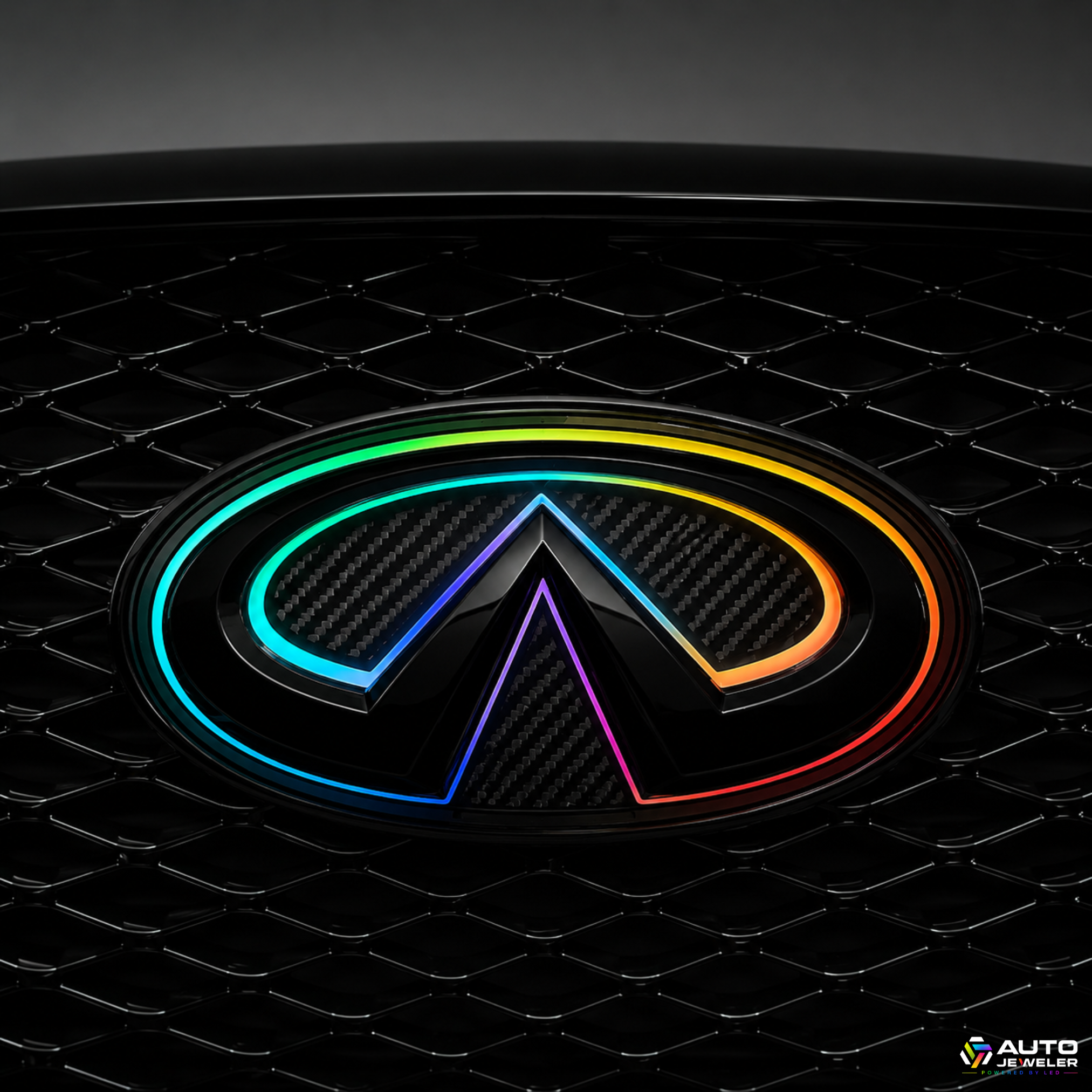 Close-up of the AutoJeweler 2018–2024 Infiniti Q50 V2 Multicolor Flow Series LED grille emblem featuring a gloss black housing, carbon fiber face, and animated RGB Flow lighting installed in the factory grille.