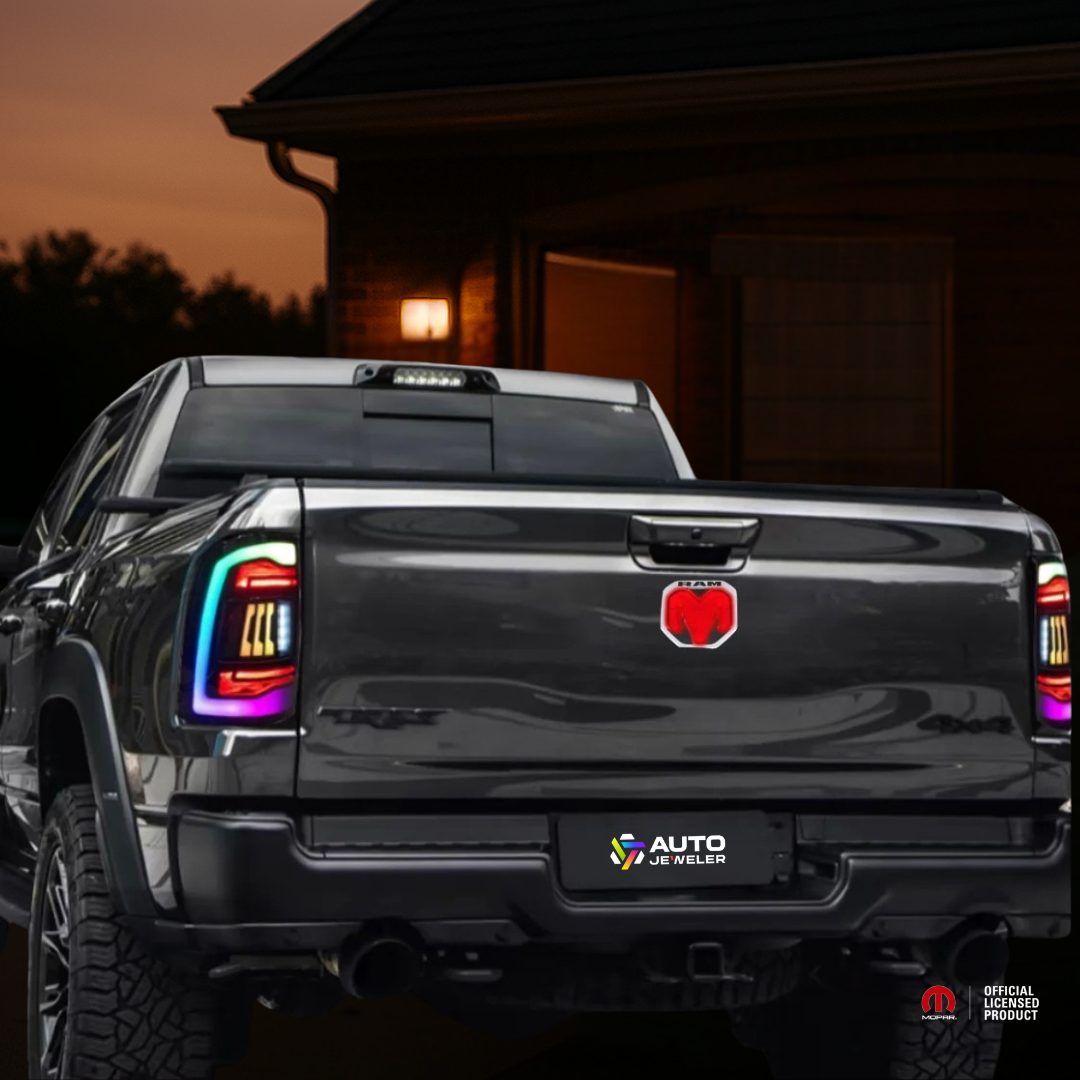 Nighttime rear shot of a RAM truck with the red LED tailgate emblem illuminated and AutoJeweler license plate branding.