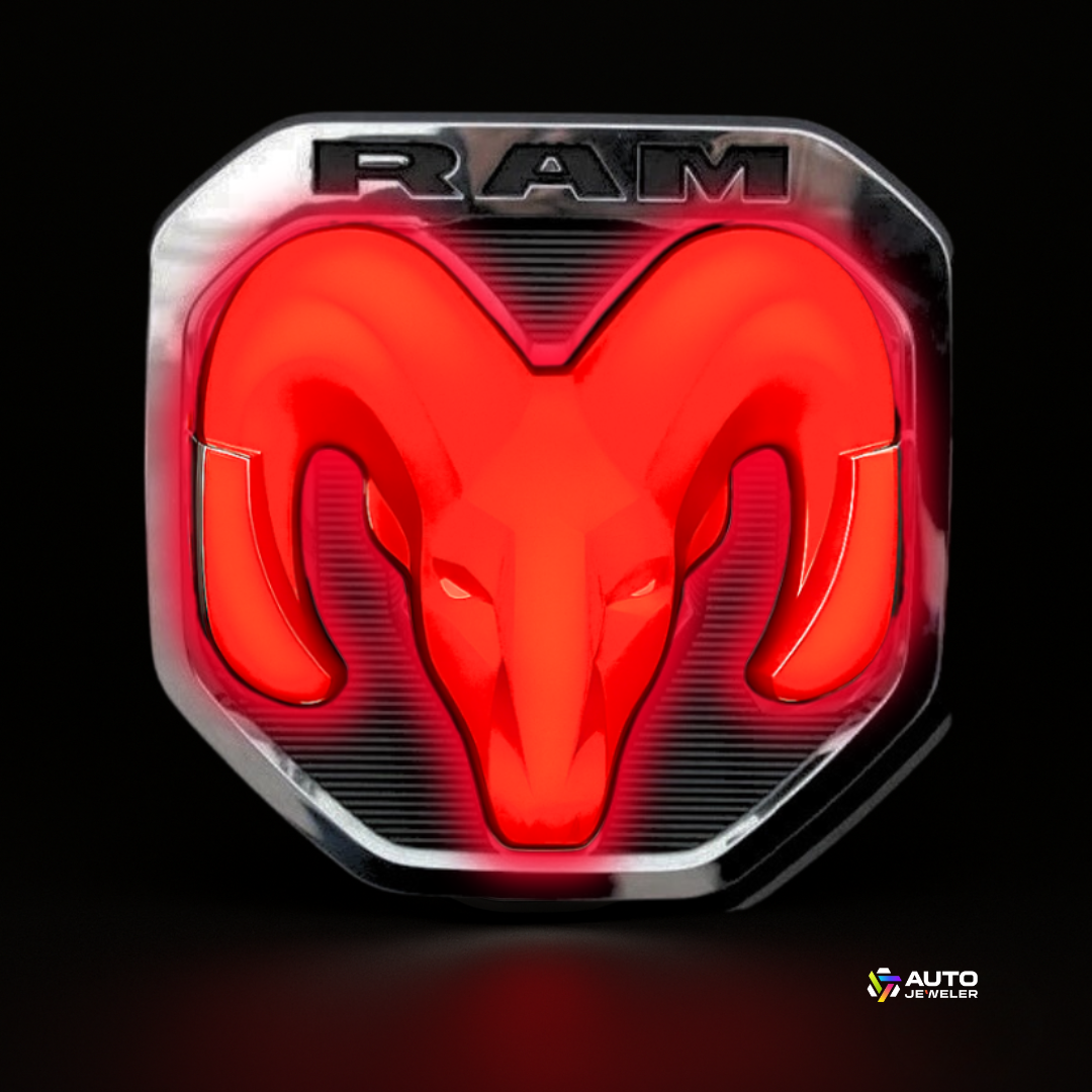Front hero shot of the 2019–2024 RAM lighted chrome/black tailgate emblem glowing bright red on a black background with AutoJeweler logo.