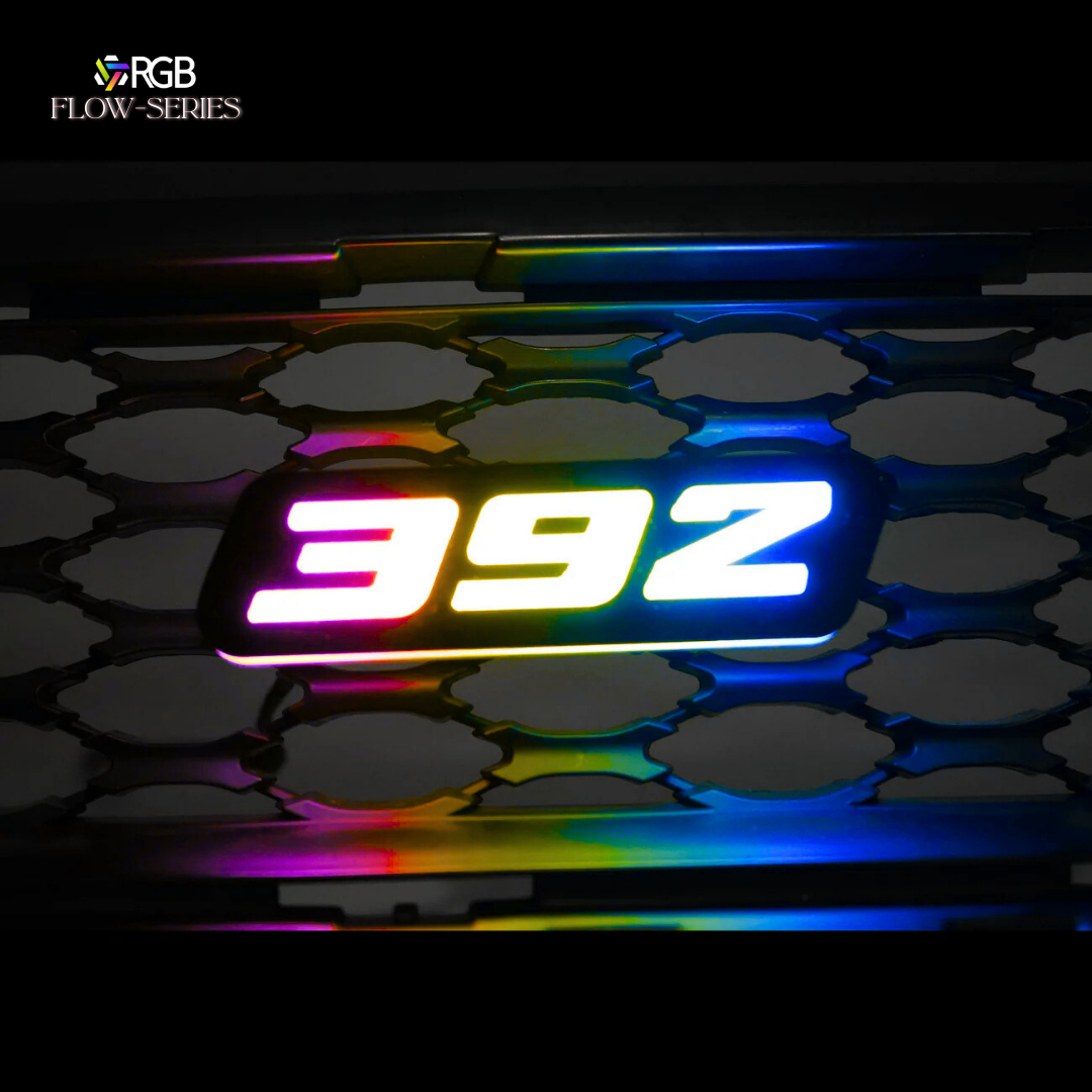 392 RGB Flow-Series LED grille emblem glowing in multicolor on a honeycomb grille – AutoJeweler hero image.