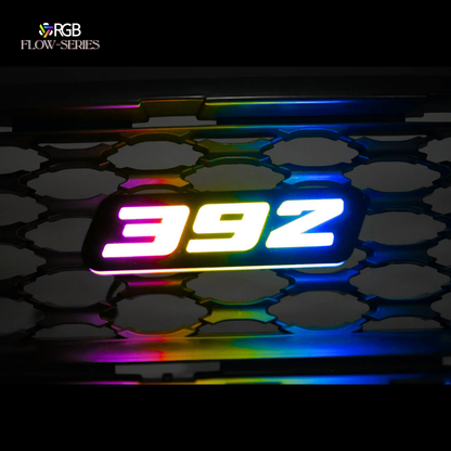 392 RGB Flow-Series LED grille emblem glowing in multicolor on a honeycomb grille – AutoJeweler hero image.