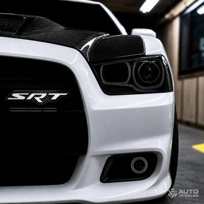 Carbon fiber SRT grille emblem installed and powered off on the black grille of a white Dodge performance vehicle.