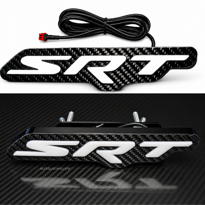 Close-up of AutoJeweler Premium Carbon Fiber SRT RGB LED grille emblem highlighting gloss carbon fiber faceplate, raised 3D white lettering, premium black housing, and included wiring harness