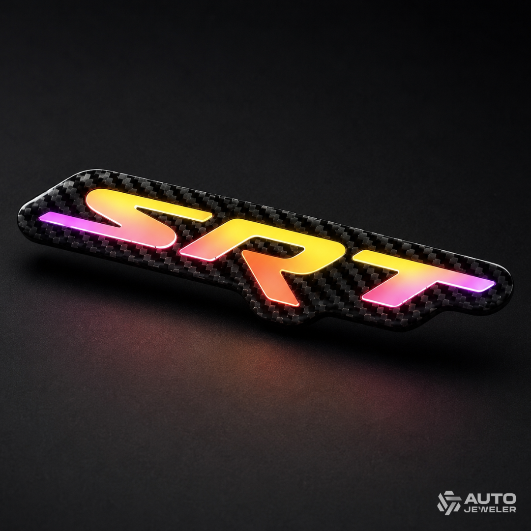 Angled product photo of an AutoJeweler carbon fiber SRT RGB LED emblem glowing amber, pink, and purple on black.