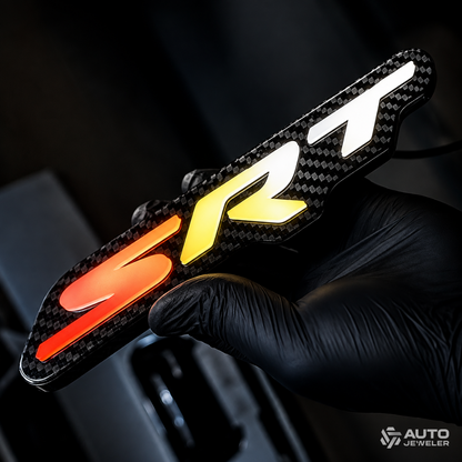 Premium carbon fiber SRT RGB LED emblem held in a black glove and glowing red, amber, yellow, and bright white.
