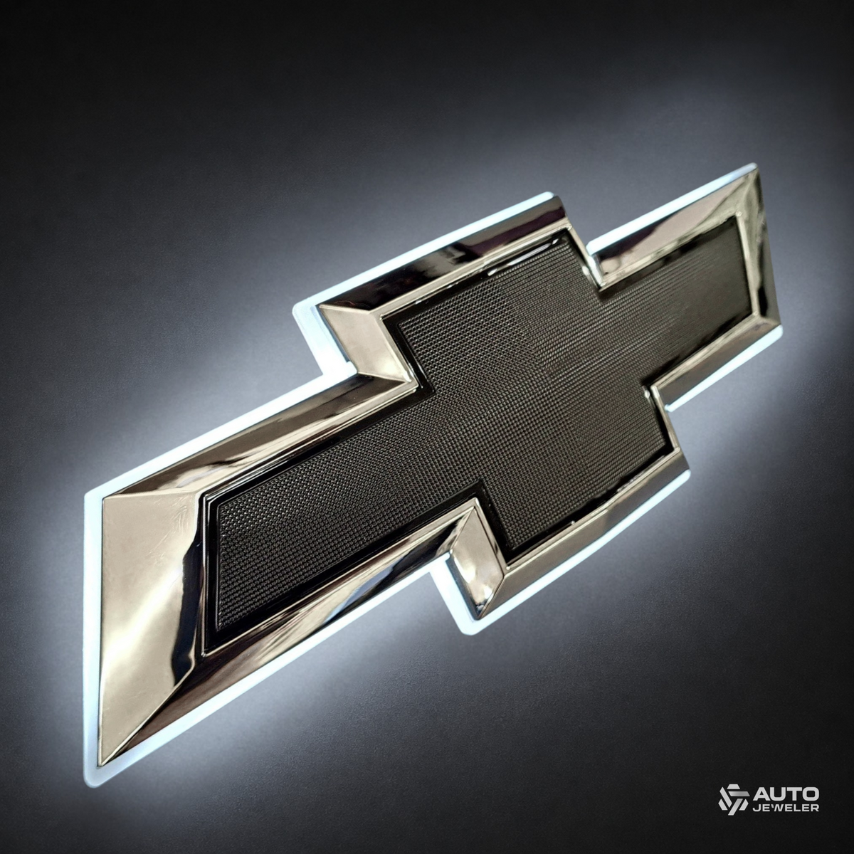 Angled view of Chevrolet chrome and black illuminated bowtie grille emblem with glowing white LED backlight