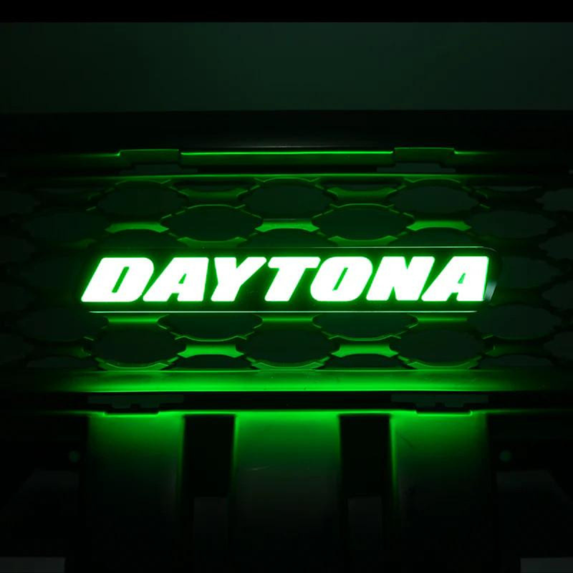 Daytona LED grille emblem illuminated in vivid green lighting mode mounted on black grille background