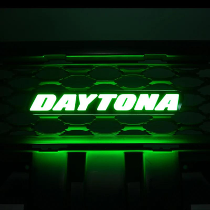 Daytona LED grille emblem illuminated in vivid green lighting mode mounted on black grille background
