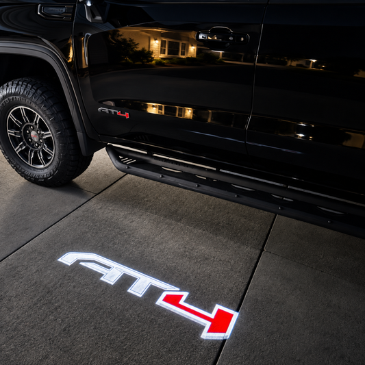 AT4 LED puddle light projecting beside a black GMC truck at night