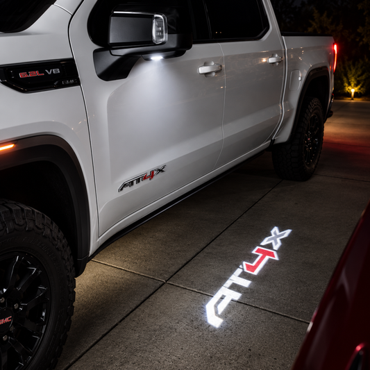 AT4X LED puddle light projection beside a white GMC truck at night
