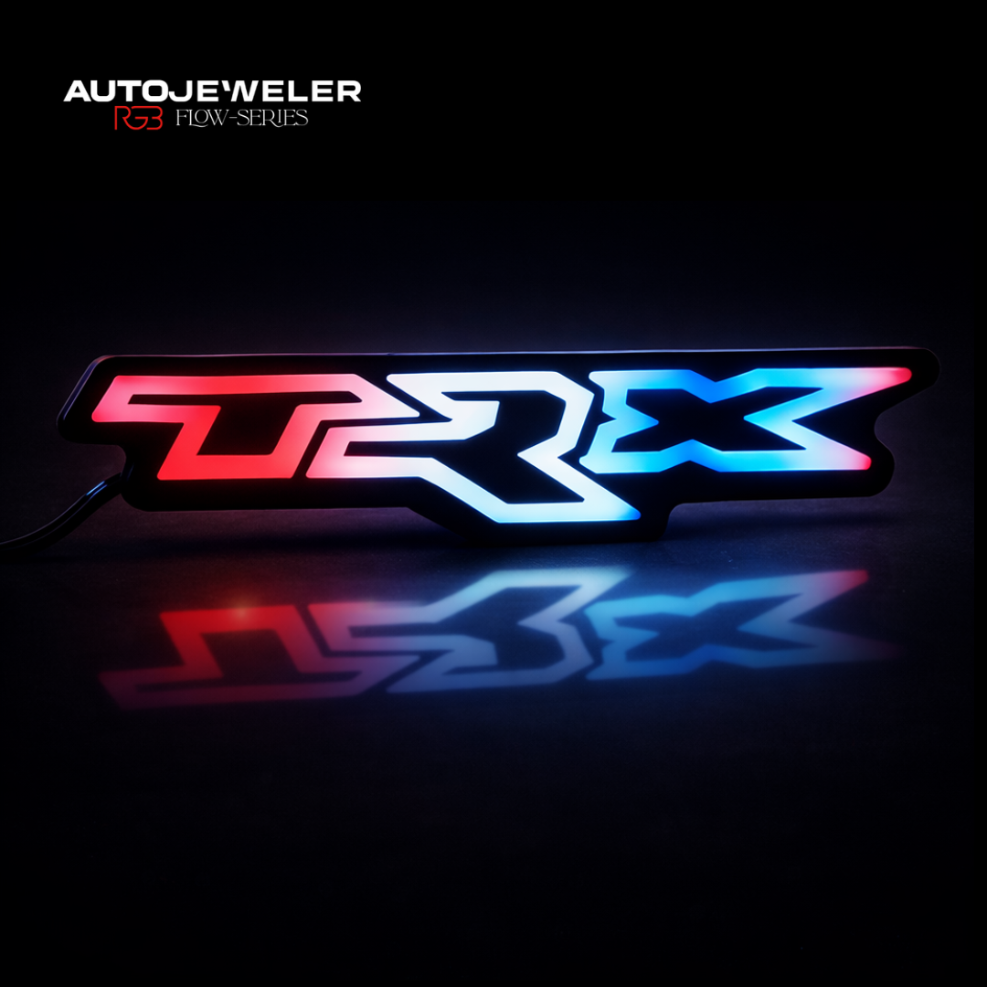 AutoJeweler RAM TRX RGB Flow Series LED grille emblem with multi-color lighting and mirrored reflection on black studio surface