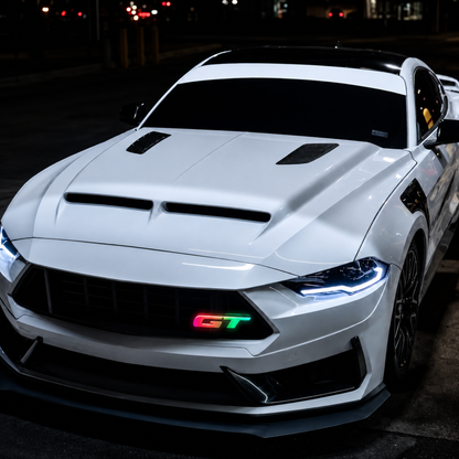 White sports car with a Flow Series illuminated LED 'GT' badge installed on the front grille glowing red and green.