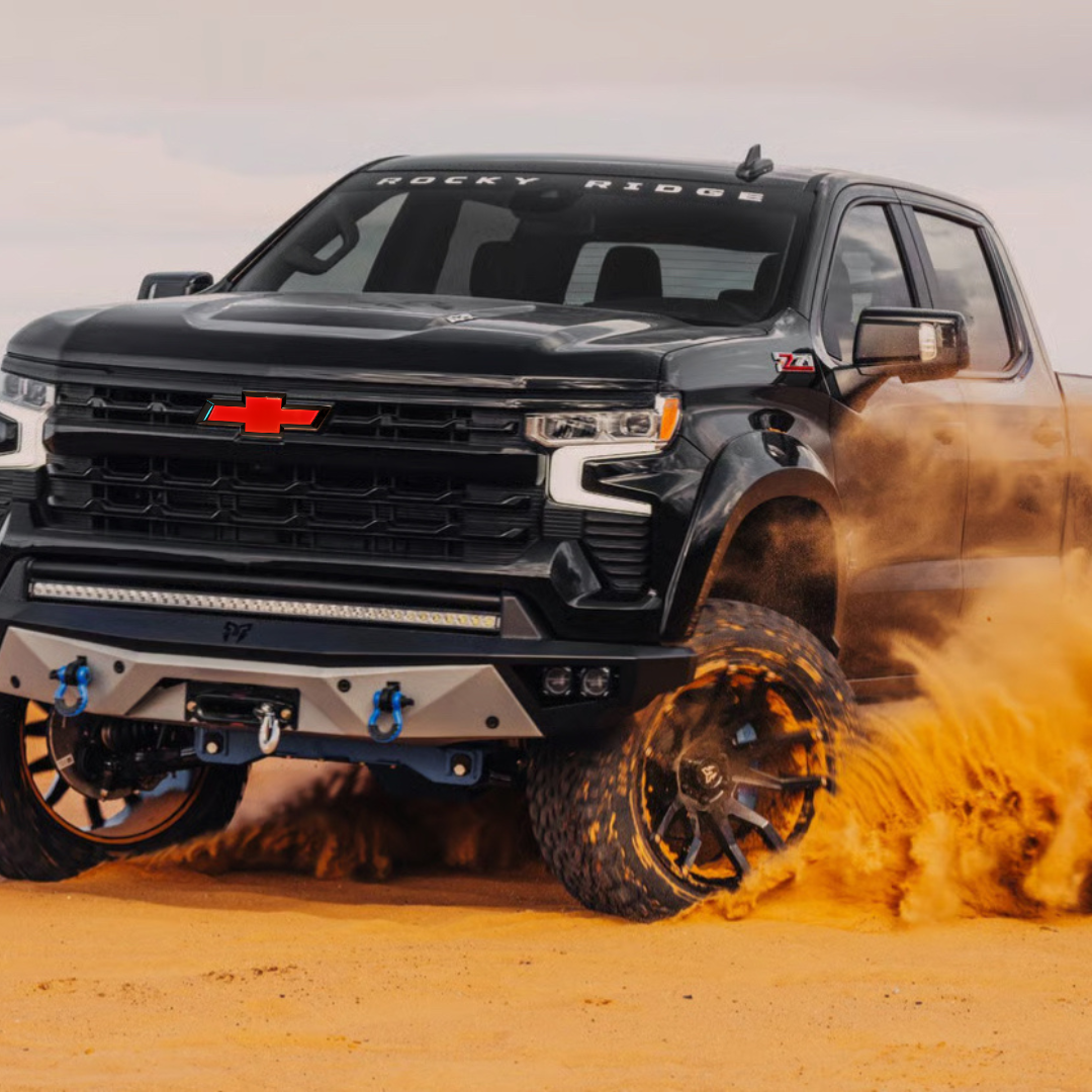 Silverado with red/black LED Bowtie emblem driving through sand — lifestyle shot