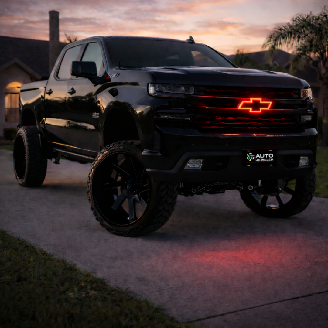 Lifted black Chevy Silverado with red RGB LED grille emblem glowing on front grille during sunset driveway photo