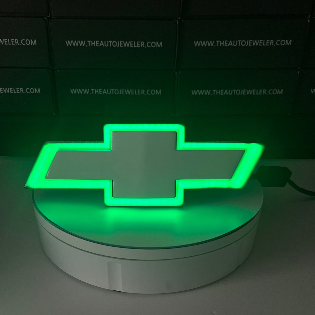Chevy Silverado RGB LED Bowtie Grille Emblem illuminated in green light on AutoJeweler display stand.