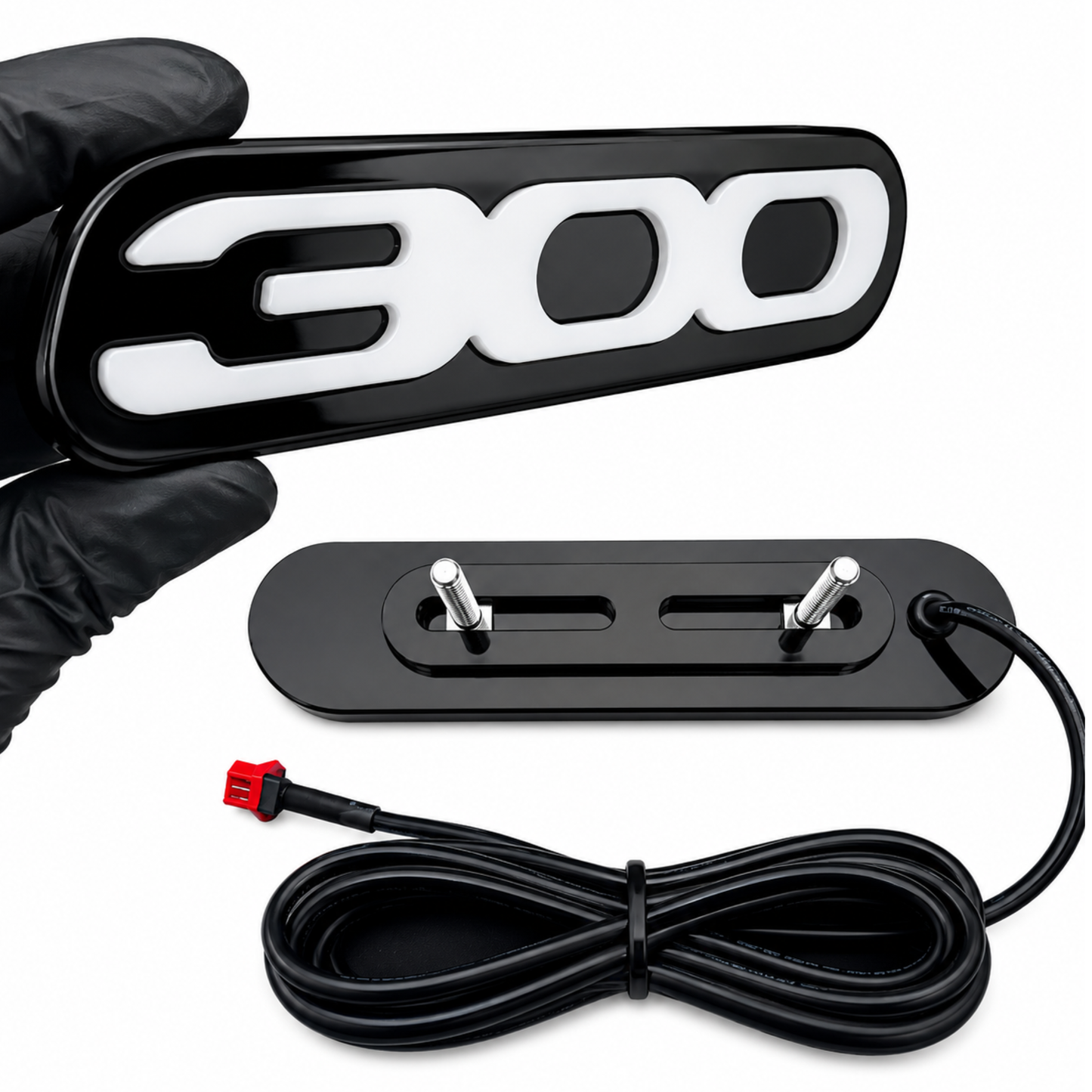 Front and rear view of Chrysler 300 LED grille emblem showing gloss black acrylic faceplate, adjustable mounting bracket, threaded studs, and plug-and-play wiring harness.