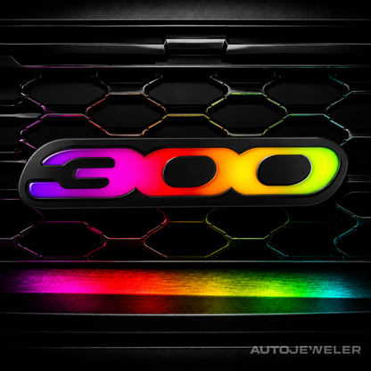 AutoJeweler Chrysler 300 LED grille emblem illuminated in RGB Flow Series rainbow mode featuring animated multicolor lighting, gloss black acrylic housing, and premium illuminated 300 badge design.