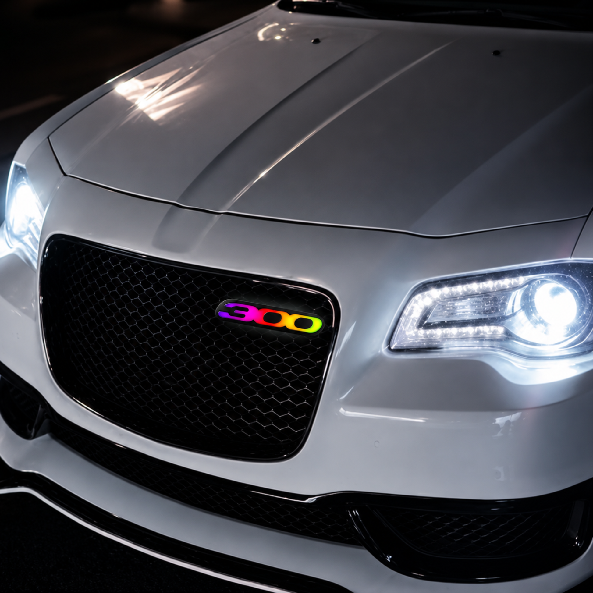 RGB Flow Series Chrysler 300 LED grille emblem installed on a white Chrysler 300 featuring vibrant rainbow illumination, custom mesh grille mounting, and luxury performance styling.
