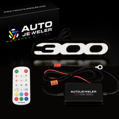Complete package contents for Chrysler 300 RGB Flow Series LED grille emblem including illuminated 300 badge, AutoJeweler R3 Flow Series controller, RF remote control, wiring harness, and branded packaging.