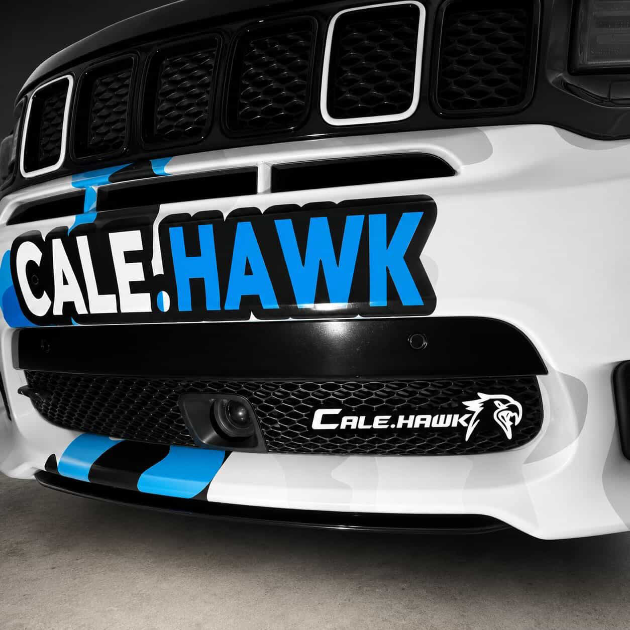 Custom Redeye Trackhawk LED grille emblem installed on a white Jeep Grand Cherokee Trackhawk with blue racing stripes.