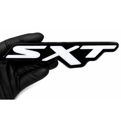 Dodge SXT RGB LED grille emblem with black housing and white face held by a gloved hand on a white background