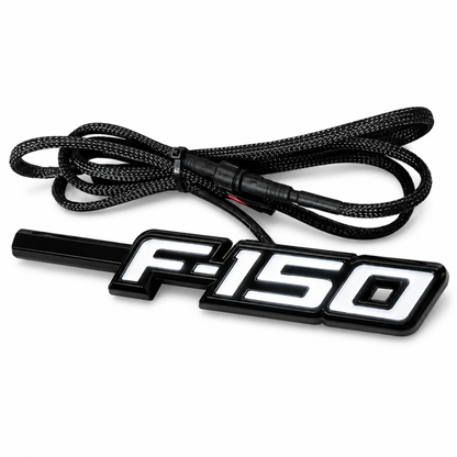 Angled view of Ford F-150 LED Fender Emblem for 2009-2014 models with black and chrome housing, white LED illumination, and integrated wiring harness.
