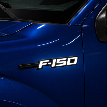 Close-up of Ford F-150 LED Fender Emblem installed on a blue 2009-2014 F-150 truck with black and chrome finish and bright white LED illumination.