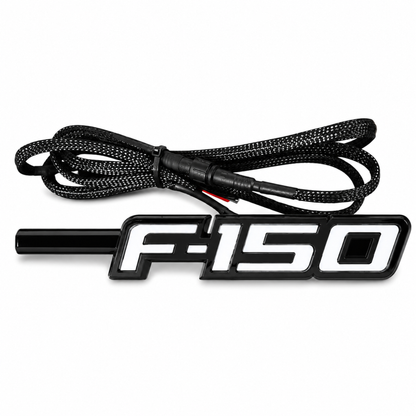 Angled view of Ford F-150 LED Fender Emblem for 2009-2014 models with black and chrome housing, white LED illumination, and integrated wiring harness.