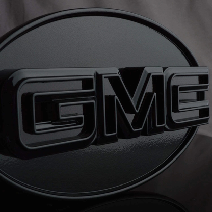 Close-up front view of gloss black GMC LED hitch cover highlighting raised GMC lettering and smooth finish