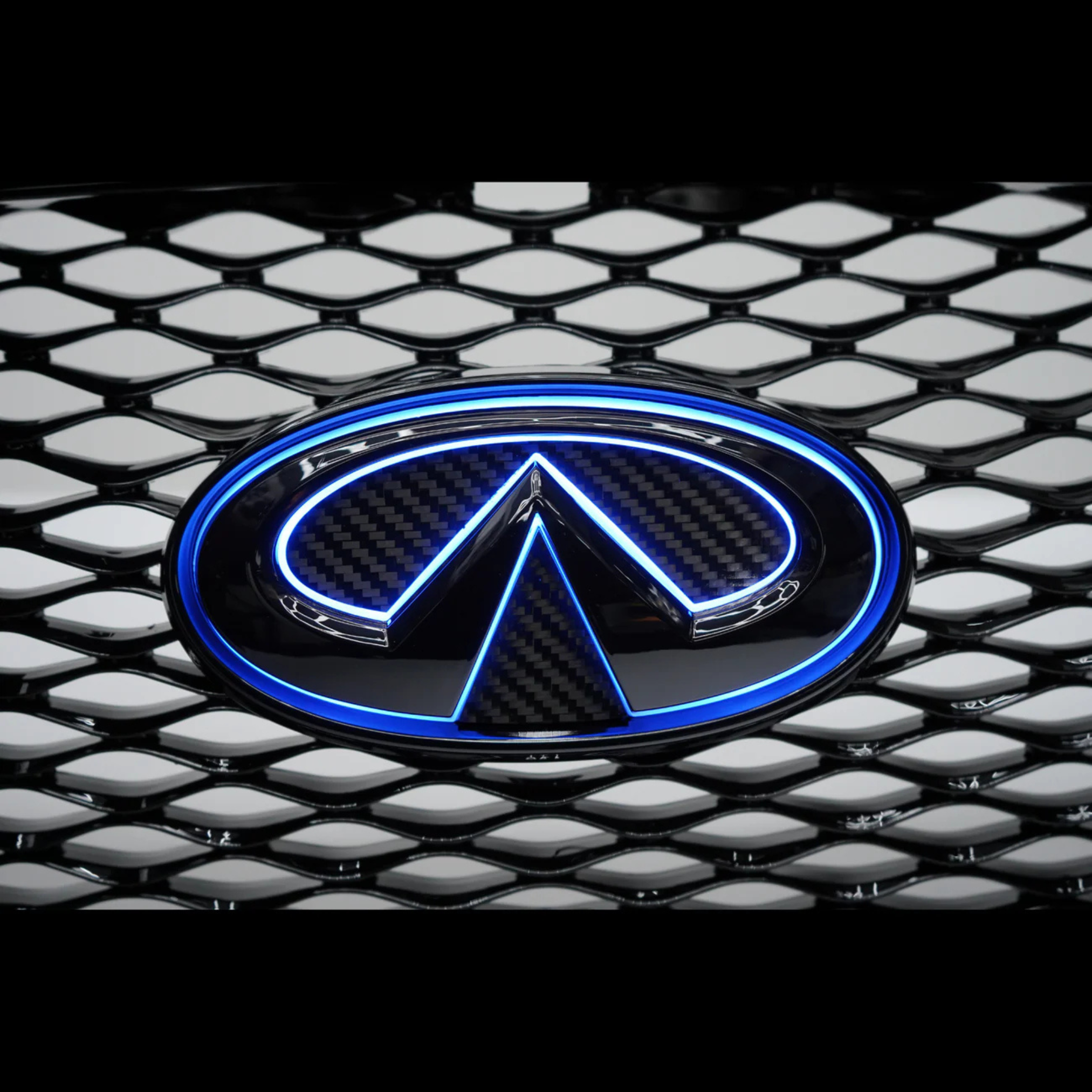 Front three-quarter view of a blue Infiniti Q50 featuring an illuminated blue LED grille emblem installed on the factory grille.