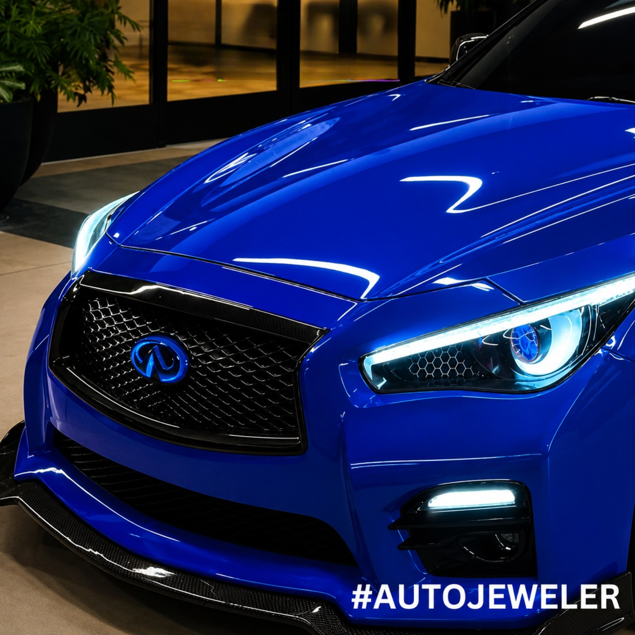 Front three-quarter view of a blue Infiniti Q50 featuring an illuminated blue LED grille emblem installed on the factory grille.