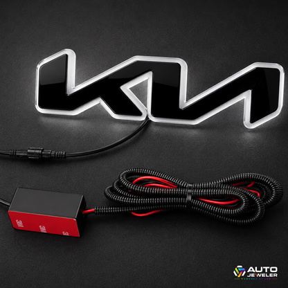 A black and silver illuminated 'KIA' emblem light with a black power cable and a red/black control box, displayed on a dark background.