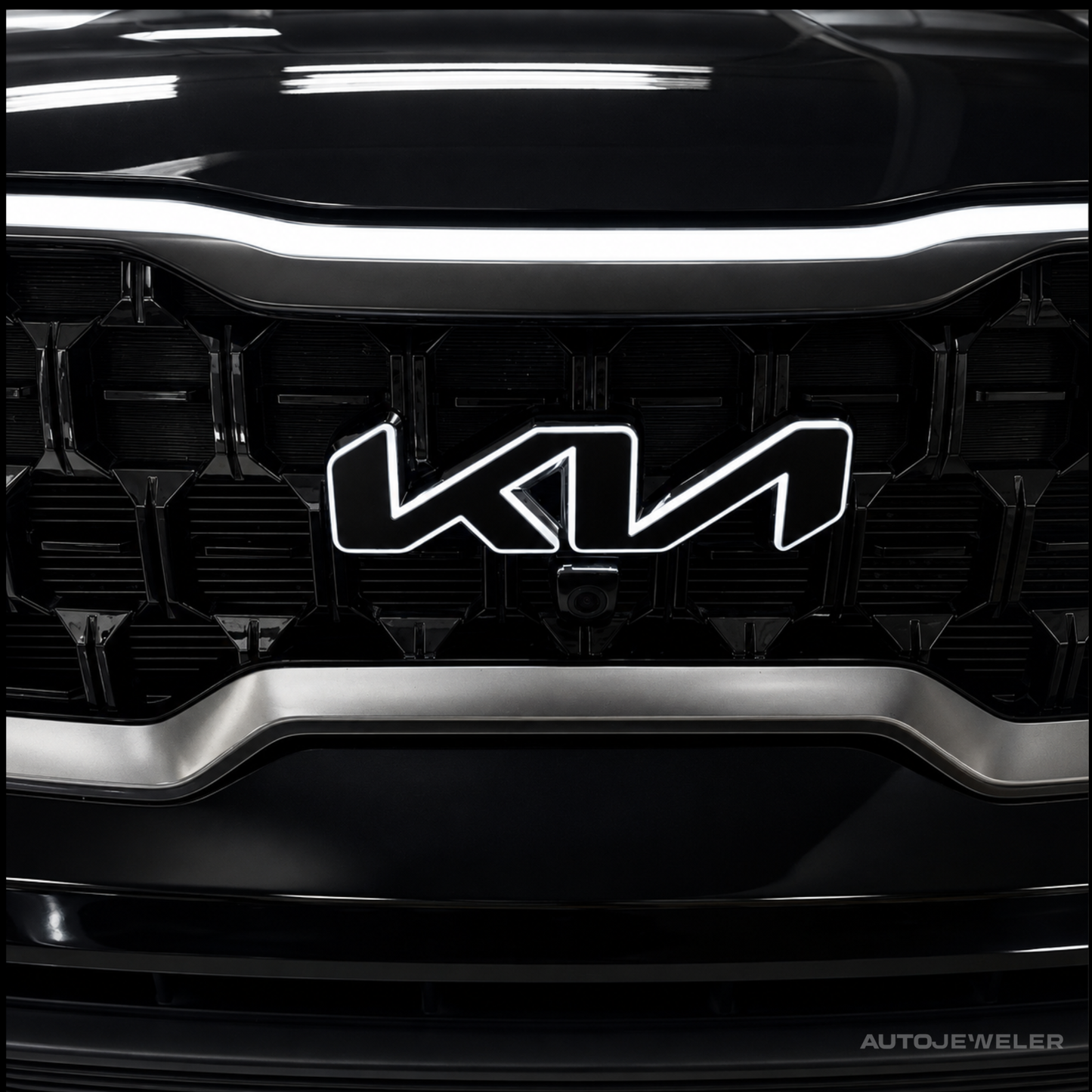 Close-up of a black car front grille with a prominent chrome-outlined Kia logo centered on the grille.