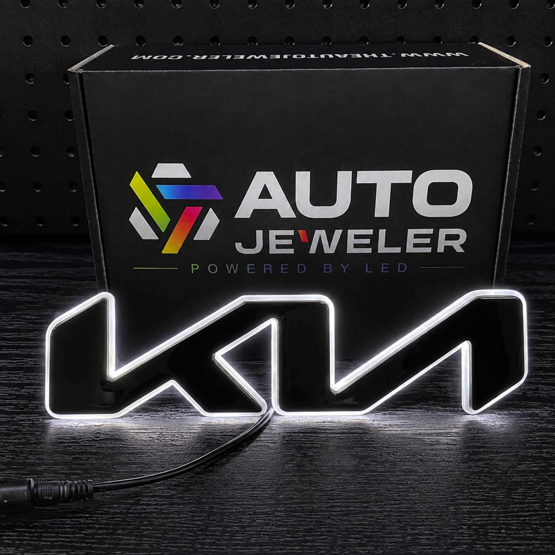 A black LED sign featuring the wordmark 'KIA' in a stylized font, illuminated with a white light border, shown in front of its black retail box branded 'AUTO JEWELER'.