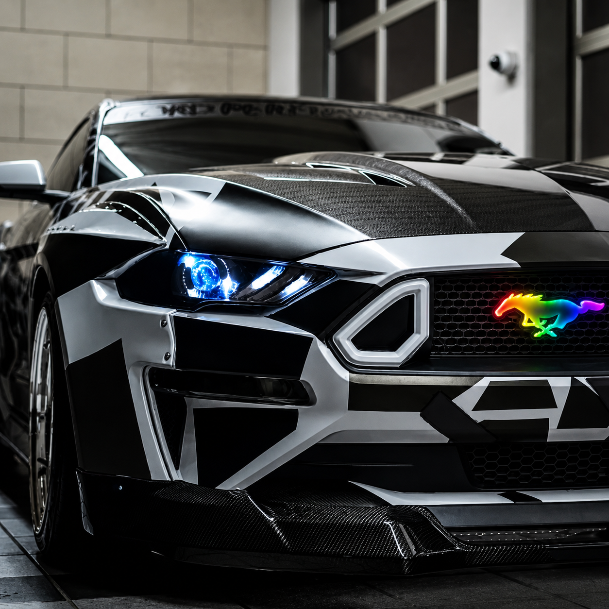 Custom Ford Mustang with AutoJeweler Flow Series RGB Pony LED grille emblem installed, featuring multicolor illuminated pony badge, aggressive front-end styling, carbon fiber accents, and premium aftermarket lighting upgrade.