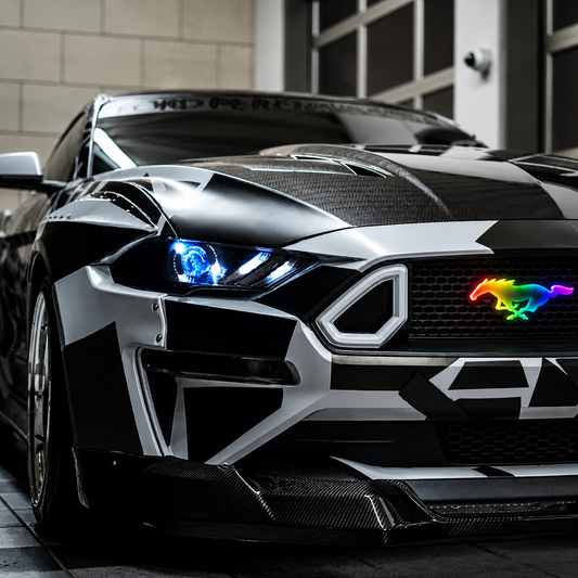 Custom Ford Mustang with AutoJeweler Flow Series RGB Pony LED grille emblem installed, featuring multicolor illuminated pony badge, aggressive front-end styling, carbon fiber accents, and premium aftermarket lighting upgrade.