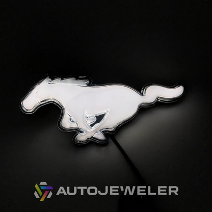 2015–2023 Ford Mustang S550 White LED illuminated pony grille emblem glowing on black background with AutoJeweler branding
