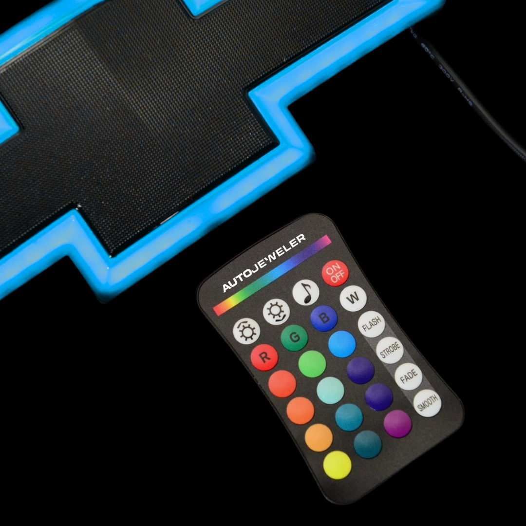 AutoJeweler RGB grille emblem glowing blue next to the included remote control.